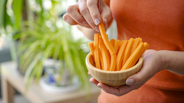 Woman holding a bowl full of fresh organic carrot sticks