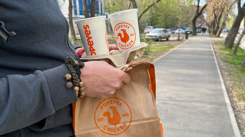 Person holding Popeyes takeout bag and drinks