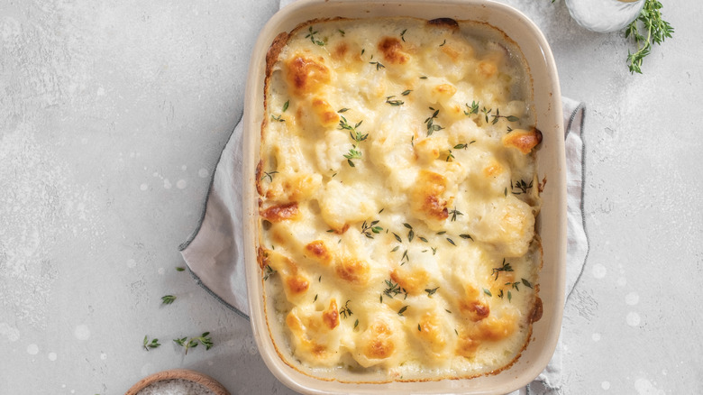 Top-down view of creamy, cheesy cauliflower in a baking dish garnished with herbs