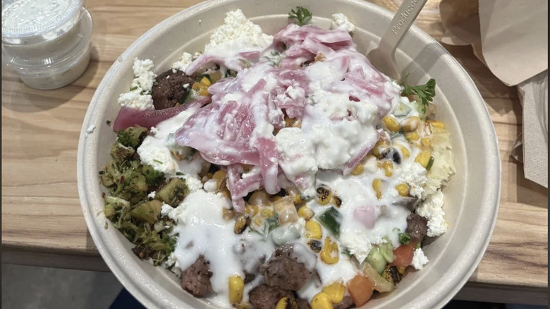 Cava bowl with a variety of toppings covered in a white sauce with two containers of sauce on the side