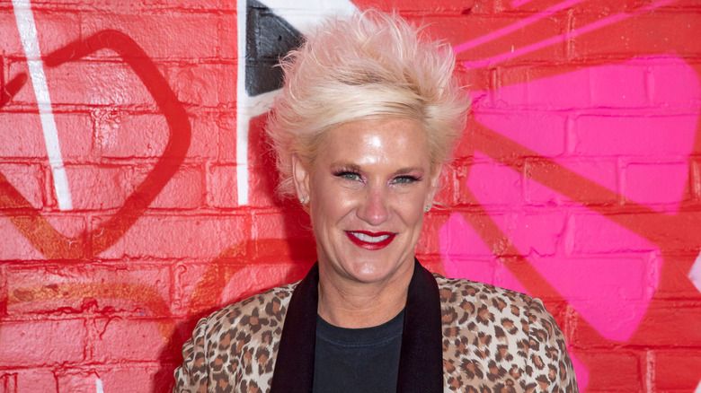 Anne Burrell standing against a bright pink and red wall
