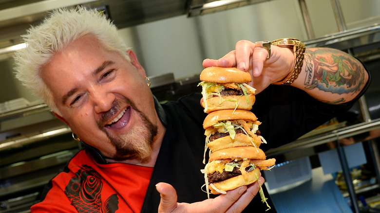 Guy Fierir holding a stack of burgers
