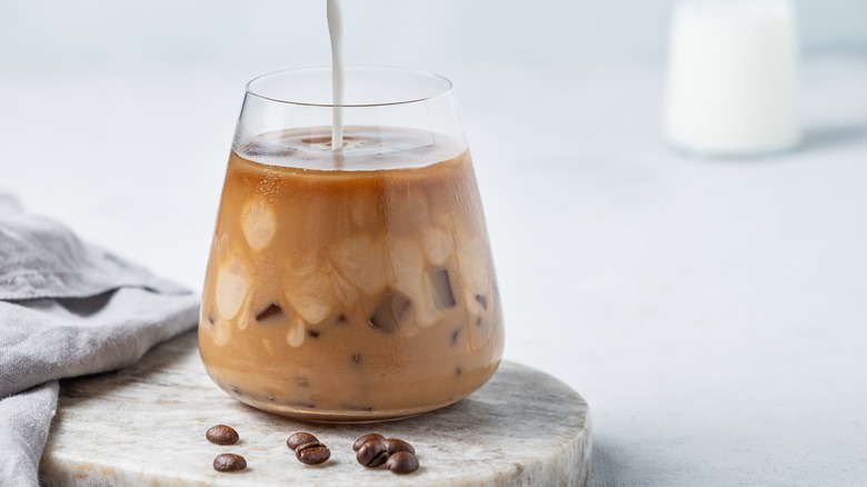 Milk pouring into a glass cup of iced coffee