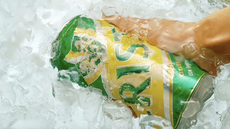 hand grabbing Cerveza Cristal can out of ice water