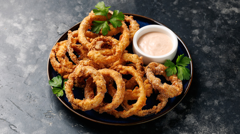 Deep fried and battered onion rings on a plate served alongside a sauce