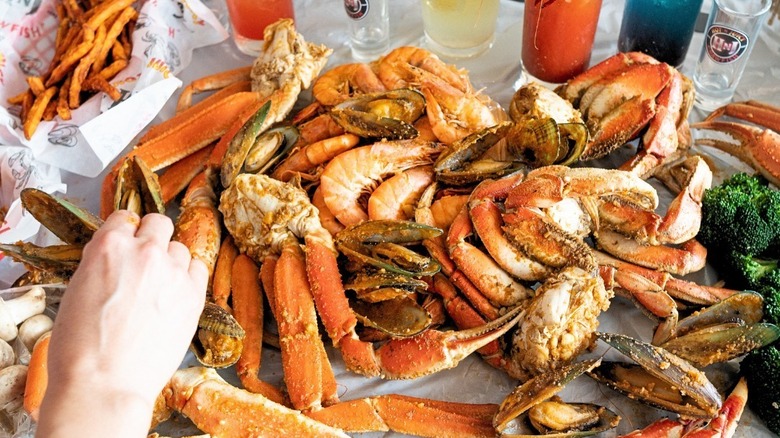 A person reaching for seafood on a table at Hot n' Juicy Crawfish