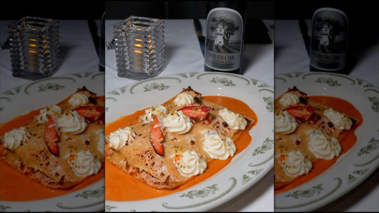 Lobster lasagna topped with lobster claw meat on platter with design.