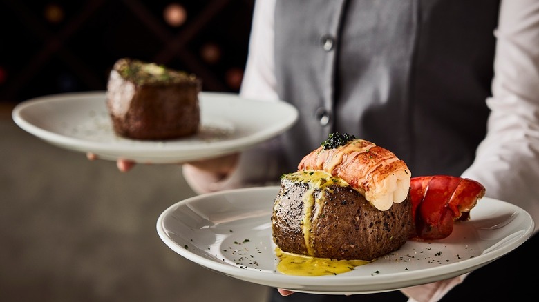 Waiter holding two plates, one with steak and one with steak and lobster tail