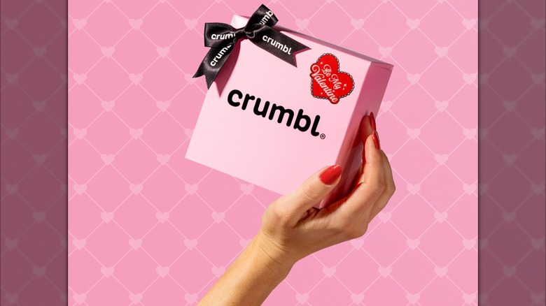 Woman's hand holding box of Crumbl cookies