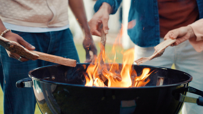 People tossing wood into a charcoal grill