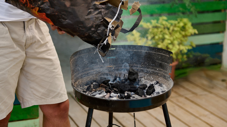 Person adding coals to grill outside on deck