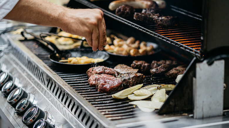 Steak, sausages, veggies, and a variety of cast iron dishes on a gas grill