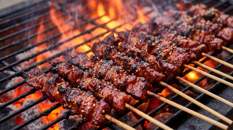 Seared barbecue meat kebabs over flaming charcoal