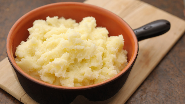 Mashed potatoes in an orange and black crock on a wooden cutting board