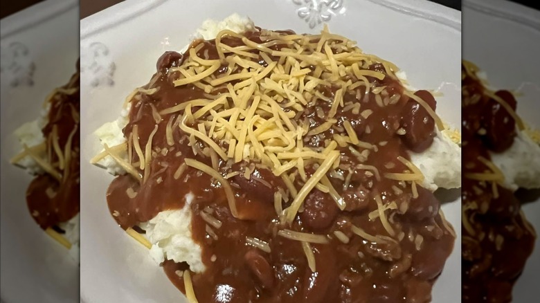 Chili over mashed potatoes with shredded cheddar cheese in a white bowl
