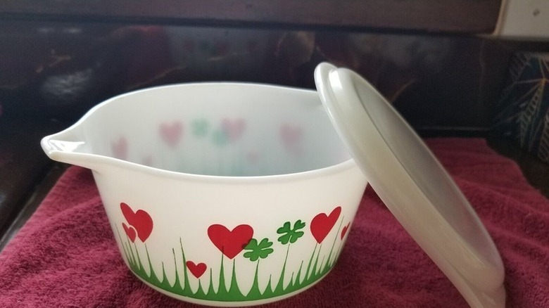 A white Pyrex container with a pattern of hearts and four-leaf clovers on it.