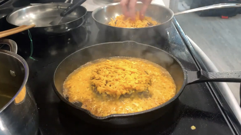 A burger cooks with a cheese skirt in a cast iron skillet