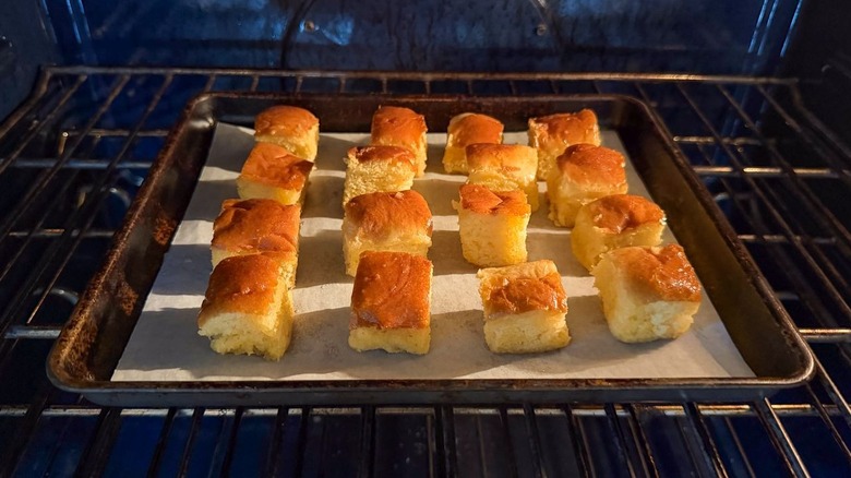 Buttered brioche cubes on parchment-lined baking sheet in oven