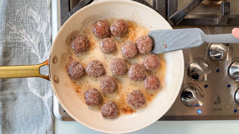 Flipping beef patties in large white skillet with spatula