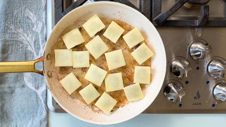 Small beef patties with white cheese squares cooking in skillet