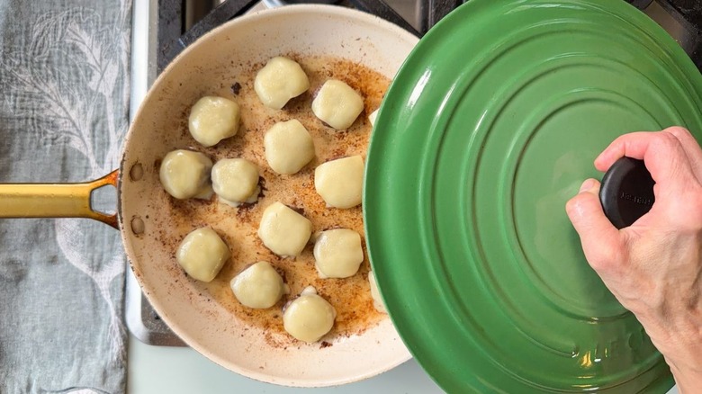Skillet with cheeseburger patties half-covered with green lid on stovetop