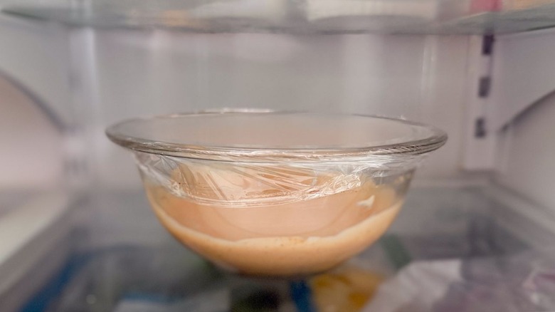 Burger sauce in plastic-covered glass bowl in refrigerator