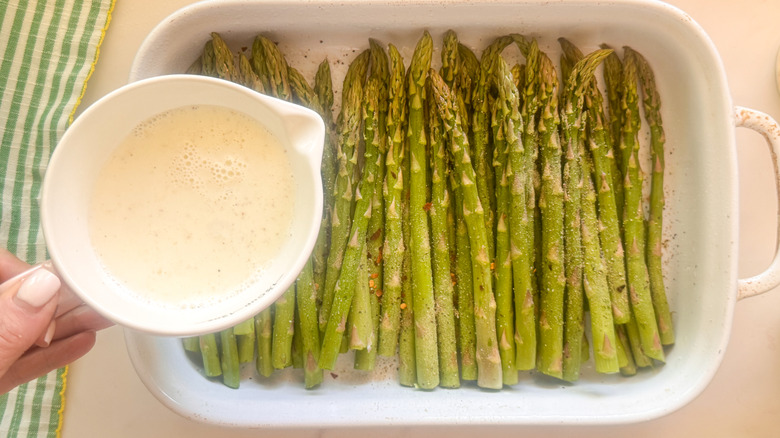 hand adding cream to asparagus