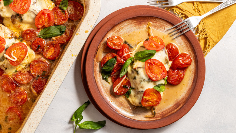 Cheesy caprese chicken bake on a plate with roasted tomatoes and basil on top