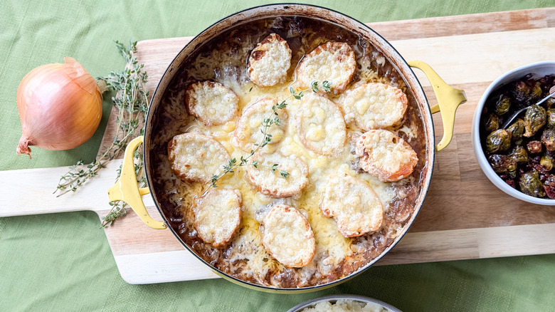 Cheesy French onion pot roast in pan on cutting board with onion and fresh thyme