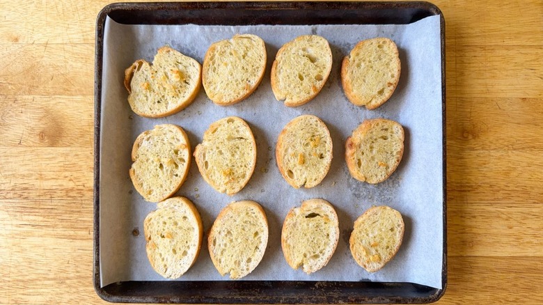 Baked baguette slices with olive oil and garlic on parchment-lined baking tray