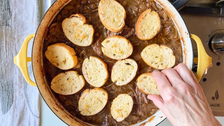 Arranging baguette croutons over French onion pot roast in large yellow pot