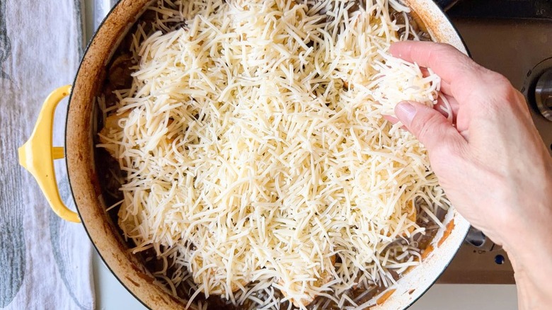Sprinkling shredded cheese over French onion pot roast in large yellow pot