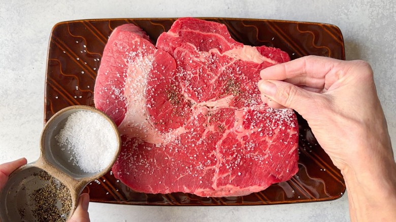 Seasoning a boneless beef roast on platter with salt and pepper