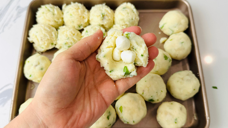 Hand holding mashed potato ball filled with mozzarella pearls