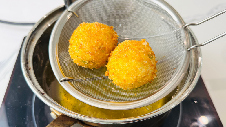 Fried mashed potato balls in strainer over pot of oil