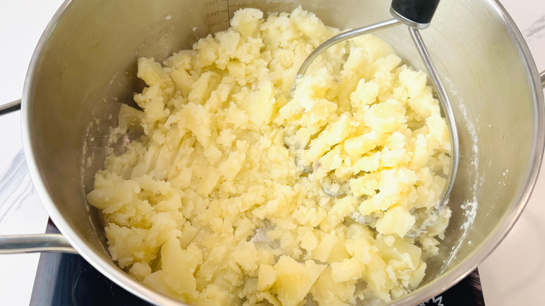 Potato masher mashing potatoes in pot