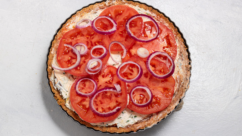 Pie crust with cream cheese filling, fresh tomatoes, and red onion rings on top