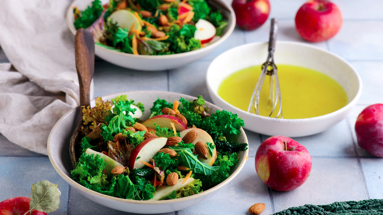 Two bowls of crisp salads beside a bowl of light dressing to be whisked.