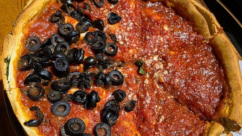 A half-and-half deep-dish pizza: one side is with olives, the other with just tomato sauce.