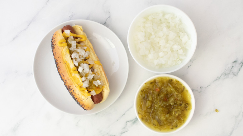 Hot dog in a bun, drizzled with mustard, and topped with onions and relish.