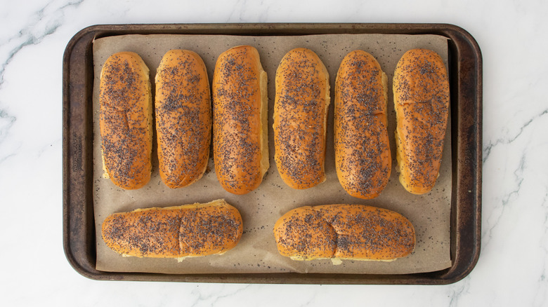 Hot dog buns sprinkled with poppyseeds on a large baking sheet