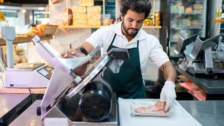 Deli worker using a meat slicer