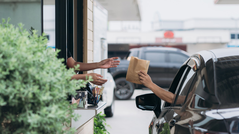 A worker passes a bag of food from a drive-thru window to someone in a car