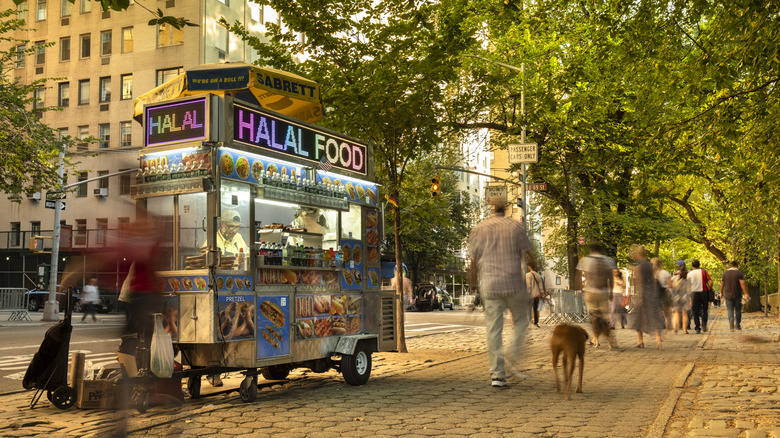 A halal cart in New York by the park with people walking by