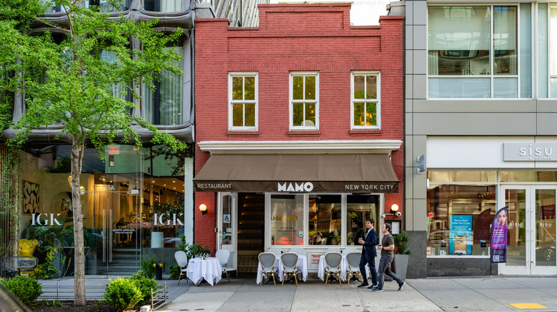 A restaurant in New York at the bottom of a brownstone with blue chairs and tables outside