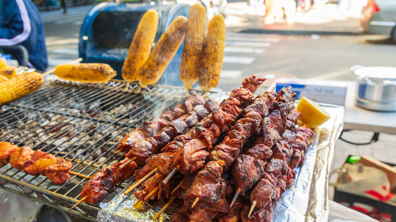 A street food cart in Jackson Heights, Queens with grilled corn and meat skewers