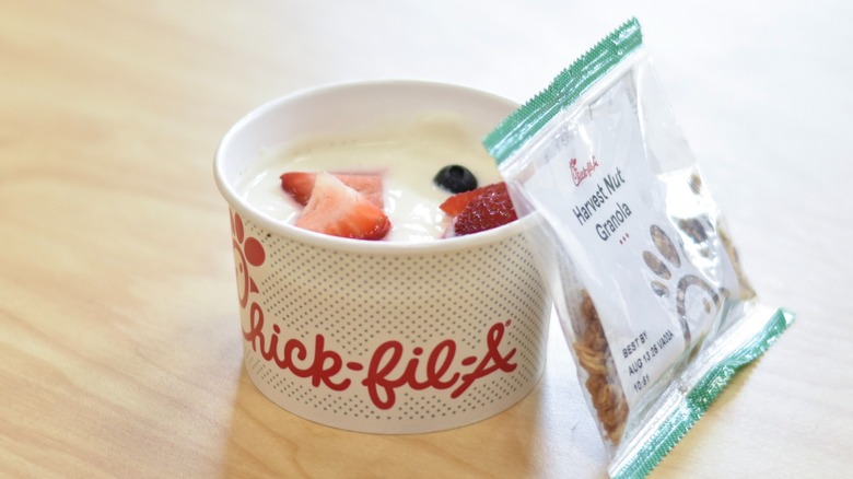 A bowl of Chick-fil-A yogurt parfait with a pack of granola on a wooden table