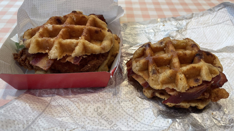 Two Chicken & Waffles Sandwiches from Chick-fil-A sit on a table with foil paper and a clamshell box.