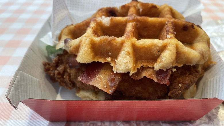 A closeup image of a Chicken & Waffles Sandwich from Chick-fil-A sitting in a clamshell box.