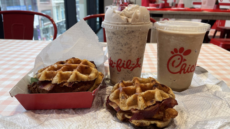 Two chicken and waffle sandwiches sit on a table with a milkshake and a blended coffee drink from Chick-fil-A.